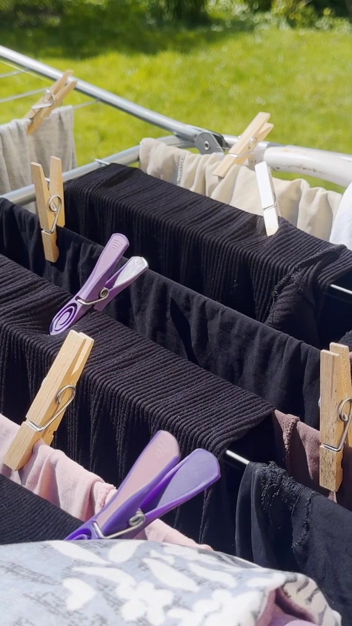 Close-up of laundry drying on an outdoor rack with wooden and purple clothespins, black ribbed fabric and sunny green garden background.