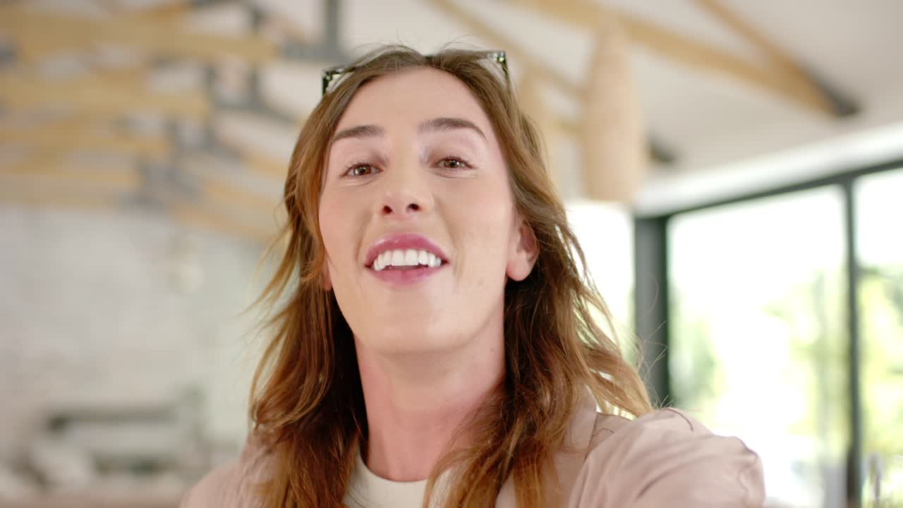 Donna che solleva il telefono, registra e parla in soggiorno, con occhiali da sole sulla testa, realizzando un vlog.