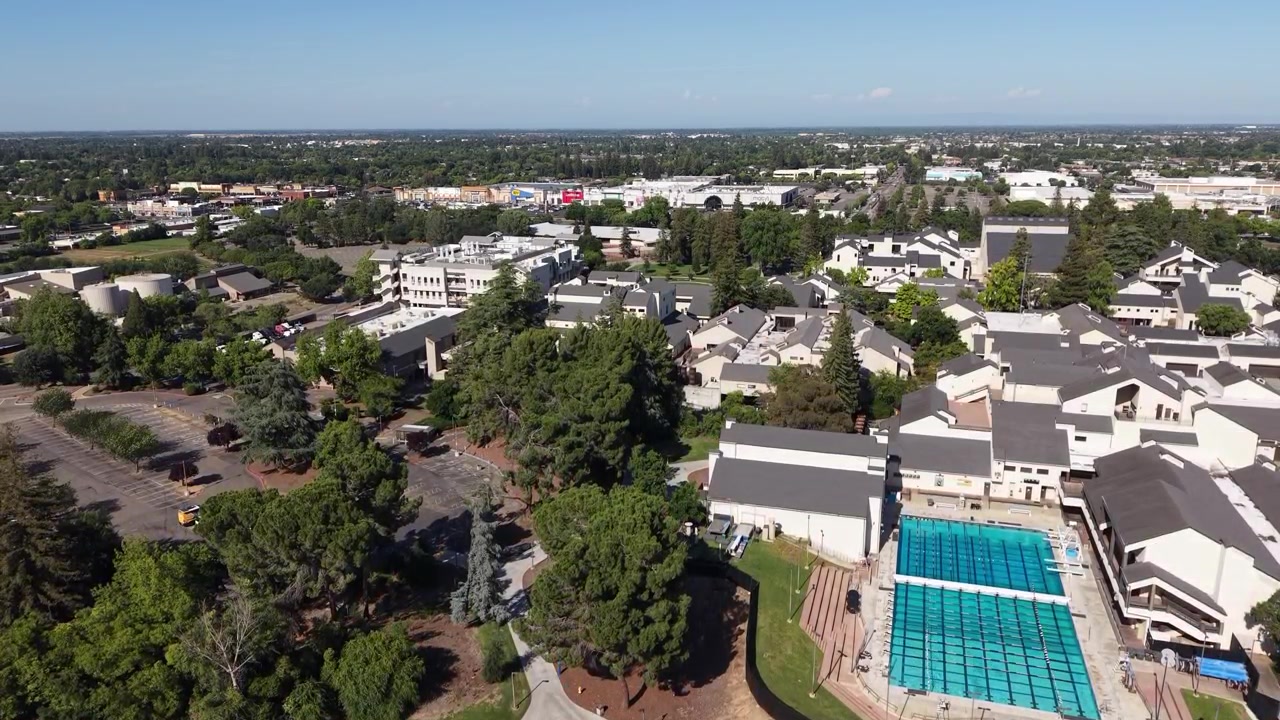 Veduta aerea del campus del San Joaquin Delta College a Stockton, California, che mostra edifici, una grande piscina e il paesaggio urbano circostante sotto un cielo azzurro e sereno in una giornata di sole.