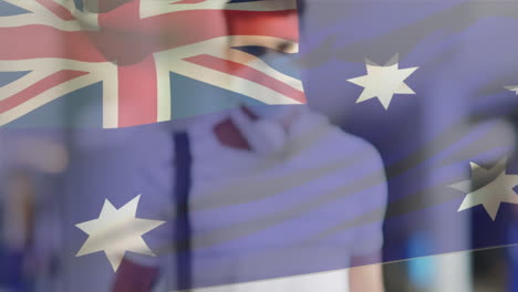 animation of flag of australia waving over man wearing face mask during covid 19 pandemic