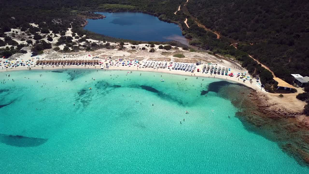 에메랄드색과 투명한 지중해의 공중 풍경, 해변에 색 해변이 가득 차 있고 해변 우산과 휴식을 취하고 목욕하는 관광객이 있습니다.