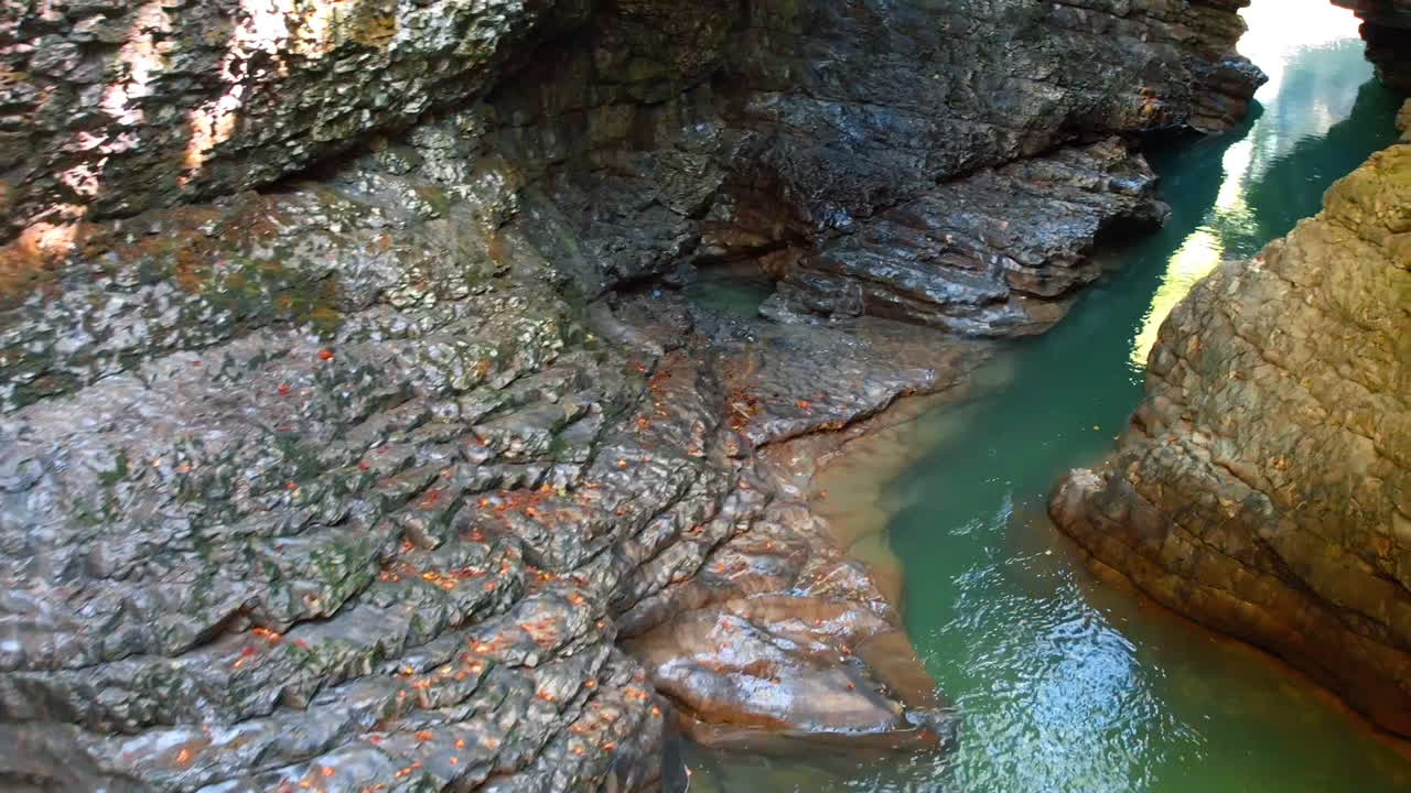 Water moves gently through a rocky canyon with steep walls. Sunlight reflects on the surface of the water. The scene shows natural beauty and texture of the rocks, creating a tranquil spot