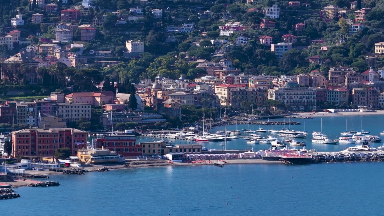 Un'ampia ripresa aerea cattura gli edifici colorati e il porto di una città costiera mediterranea.