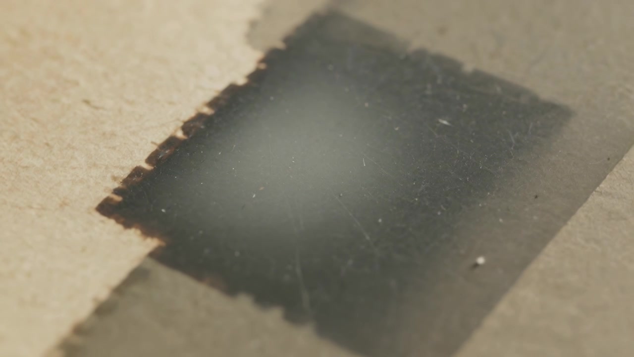 Shifting focus, lens revealing black patch with jagged edge on kraft board, checking dust and speck