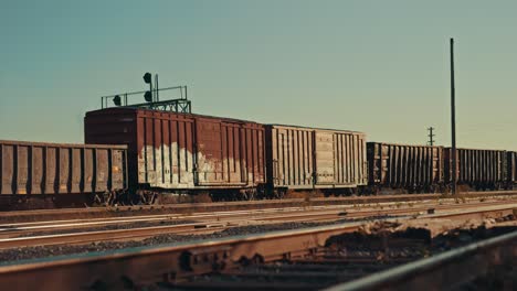 freight train cargo cars coming to a stop at empty industrial city railway yard. locomotive wagons park on station rail tracks infrastructure at sunset during golden hour dusk cinematic prores 4k