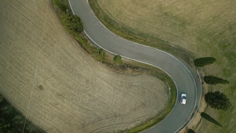 aerial top down bird's eye view of suv driving along winding road in tuscany italy