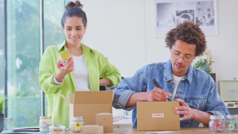 Pareja-Que-Dirige-Negocios-En-Línea-Desde-Casa-Empacando-Y-Etiquetando-Velas-Boutique-Listas-Para-Enviar