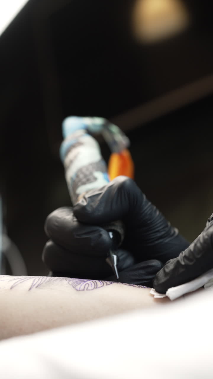 Vertical handheld shot of tattoo artist tattooing a woman's forearm, interior