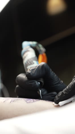 vertical handheld shot of tattoo artist tattooing a woman's forearm, interior