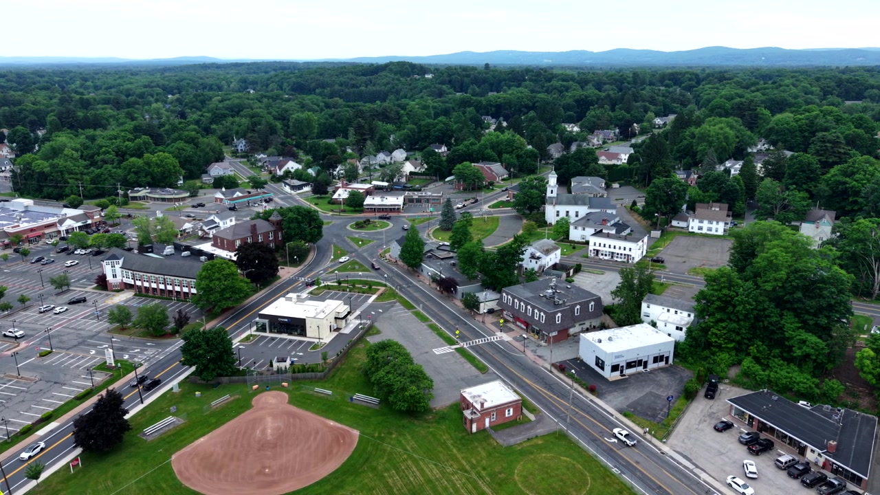 Ripresa grandangolare con drone che si sposta a destra sopra la rotatoria del Municipio di East Longmeadow, rivelando una comunità suburbana del New England e viste sulle montagne.