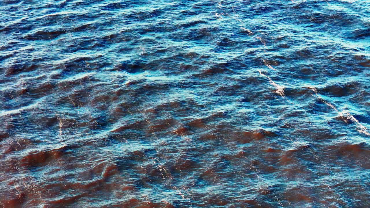 Close view of vibrant blue sea surface rippling with waves and shimmering highlights, forming striking abstract textures and motion under bright daylight