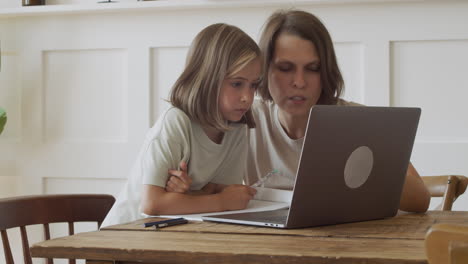 a blonde girl and her mother read the screen of a laptop with great concentration