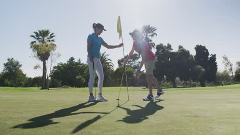 Two-caucasian-women-playing-golf-one-reaching-for-ball