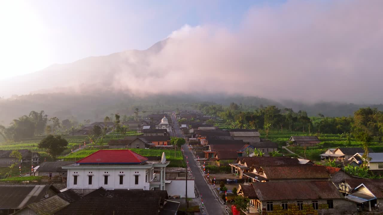Drone view of picturesque rural community and lush farmlands with foggy mountain peak in the morning. Village on the slope of Merapi volcanic mountain, Indonesia