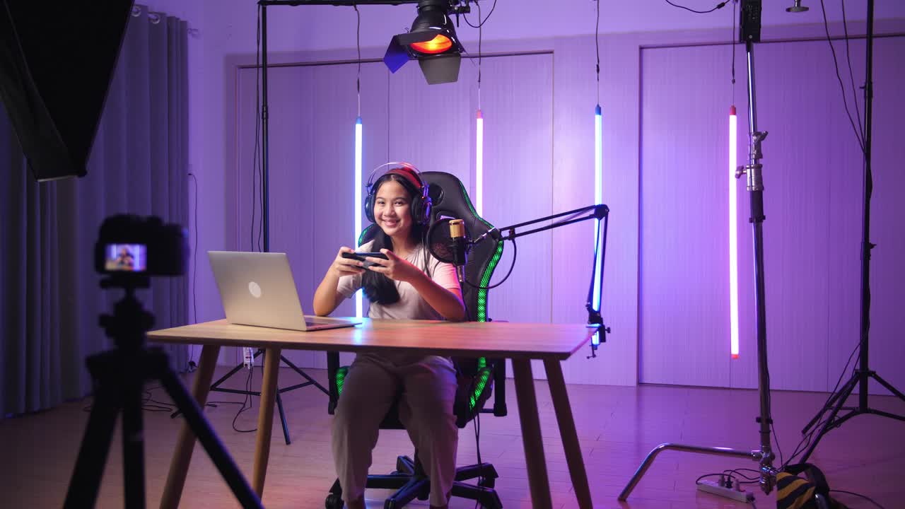 Excited Asian Kid Girl Playing Video Game With Mobile Phone Then Smiles To Camera While Live Stream, Professional Light Equipment