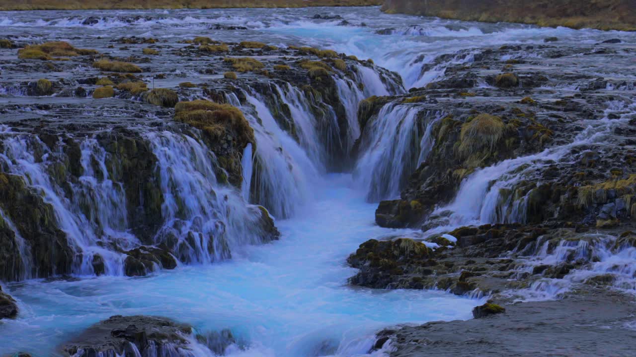 gran toma de agua azul islandesa de las cataratas del puente cayendo por las rocas cubiertas de maleza por la noche