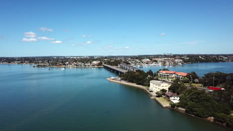 Aerial:-Drone-flying-over-water-towards-a-bridge-to-slowly-reveal-traffic-driving-over-in-Sydney,-NSW