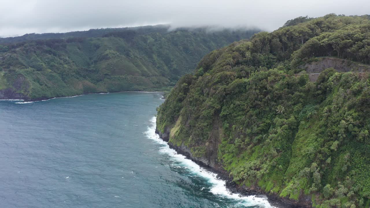 Aerial close-up shot flying over the steep jungle cliffs along the rugged coastline of the Road to Hana in Maui, Hawai'i