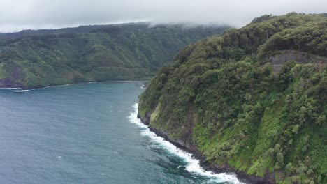 aerial close-up shot flying over the steep jungle cliffs along the rugged coastline of the road to hana in maui, hawai'i