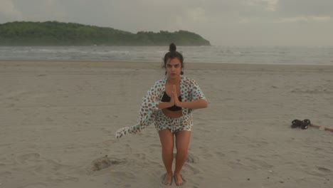 An-Indian-woman-gracefully-practices-yoga-on-a-serene-tropical-beach,-blending-her-movements-with-the-tranquil-rhythm-of-the-sea