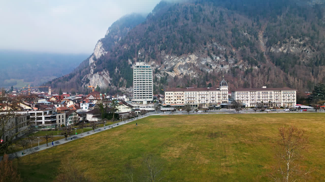 el avión no tripulado se eleva sobre los árboles sin hojas para revelar el hotel y las casas de interlaken, suiza, en un día nublado.