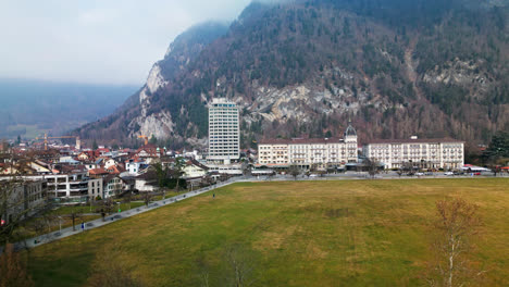 el avión no tripulado se eleva sobre los árboles sin hojas para revelar el hotel y las casas de interlaken, suiza, en un día nublado.
