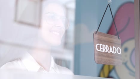happy small business girl changing closed to open sign in spanish, smiling looking outside waiting for clients. start-up concept. 4k 60fps