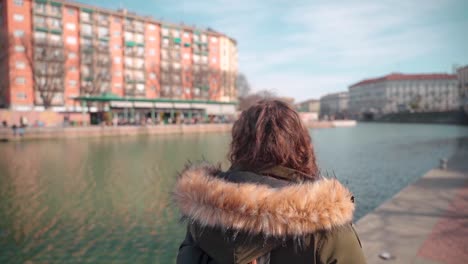 young anonymous woman with curls walks along canal system milan
