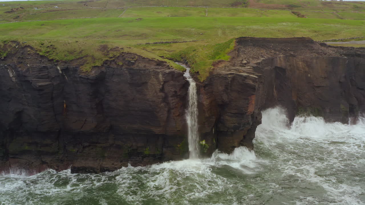 Static aerial of Cliffs of Moher waterfall and waves crashing on dark cliff faces at Doolin