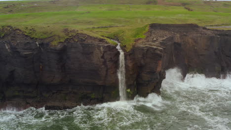 static aerial of cliffs of moher waterfall and waves crashing on dark cliff faces at doolin