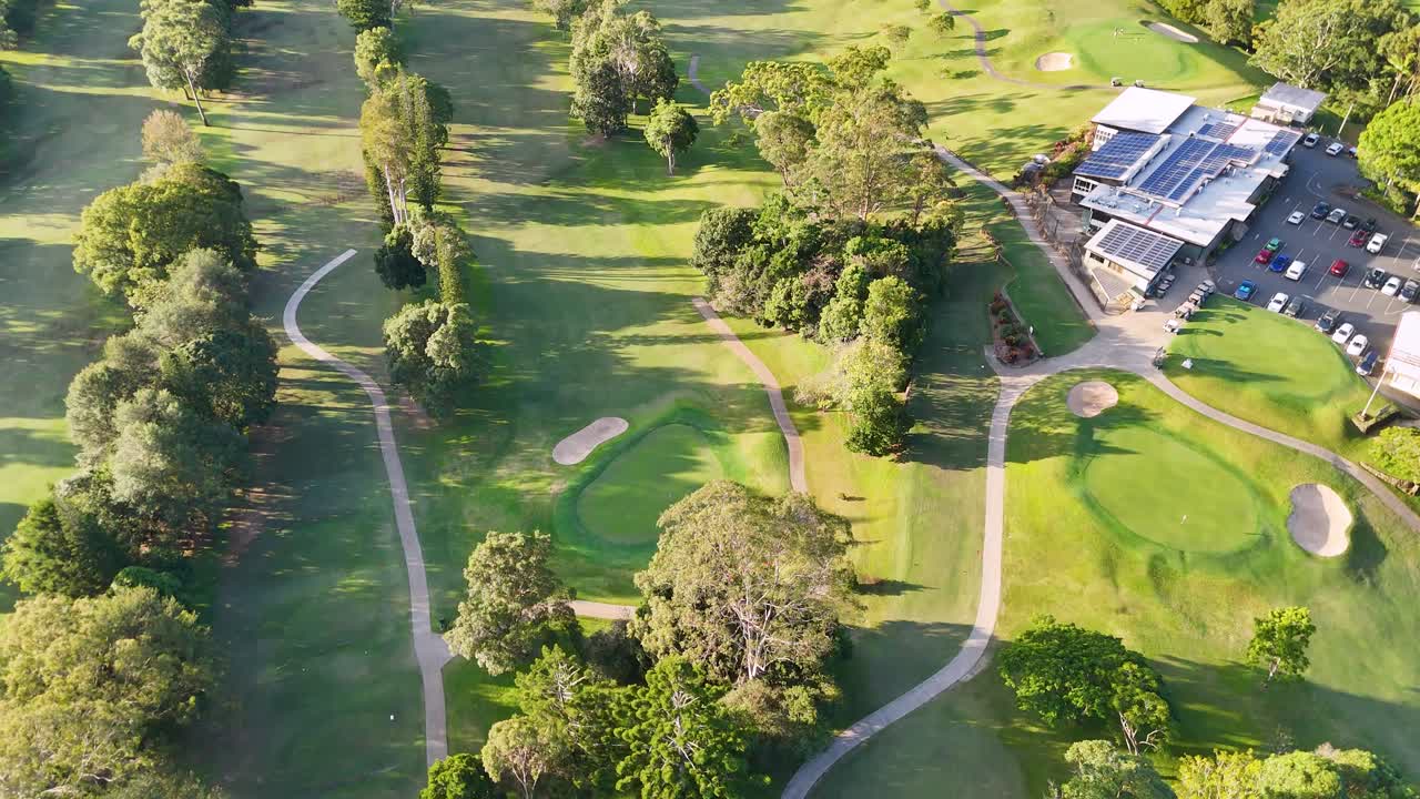 Drone captures expansive golf course with lush greenery, clubhouse, and solar panels under bright sunlight