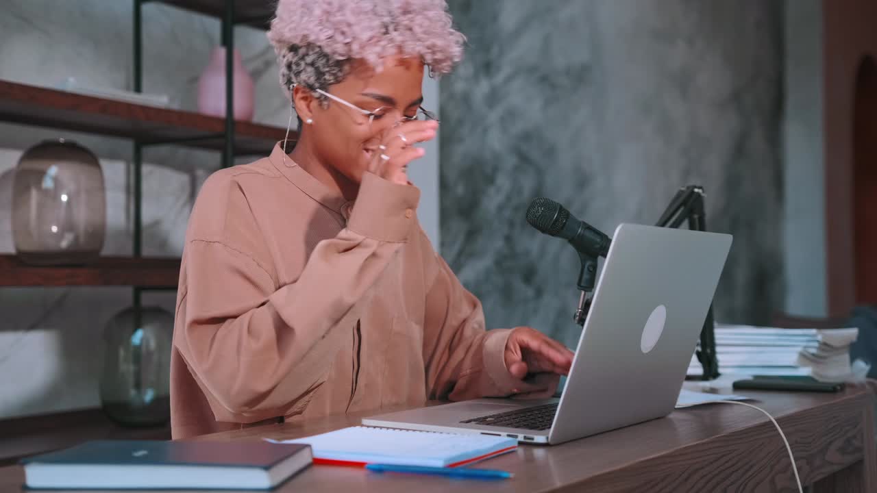 Young african american woman with smile waving hands sits at table with laptop