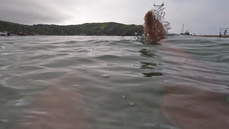 POV-man-floating-on-his-back-in-the-ocean-with-legs-and-feet-sticking-out-of-the-water,-in-Lulworth-Cove,-Dorset,-England