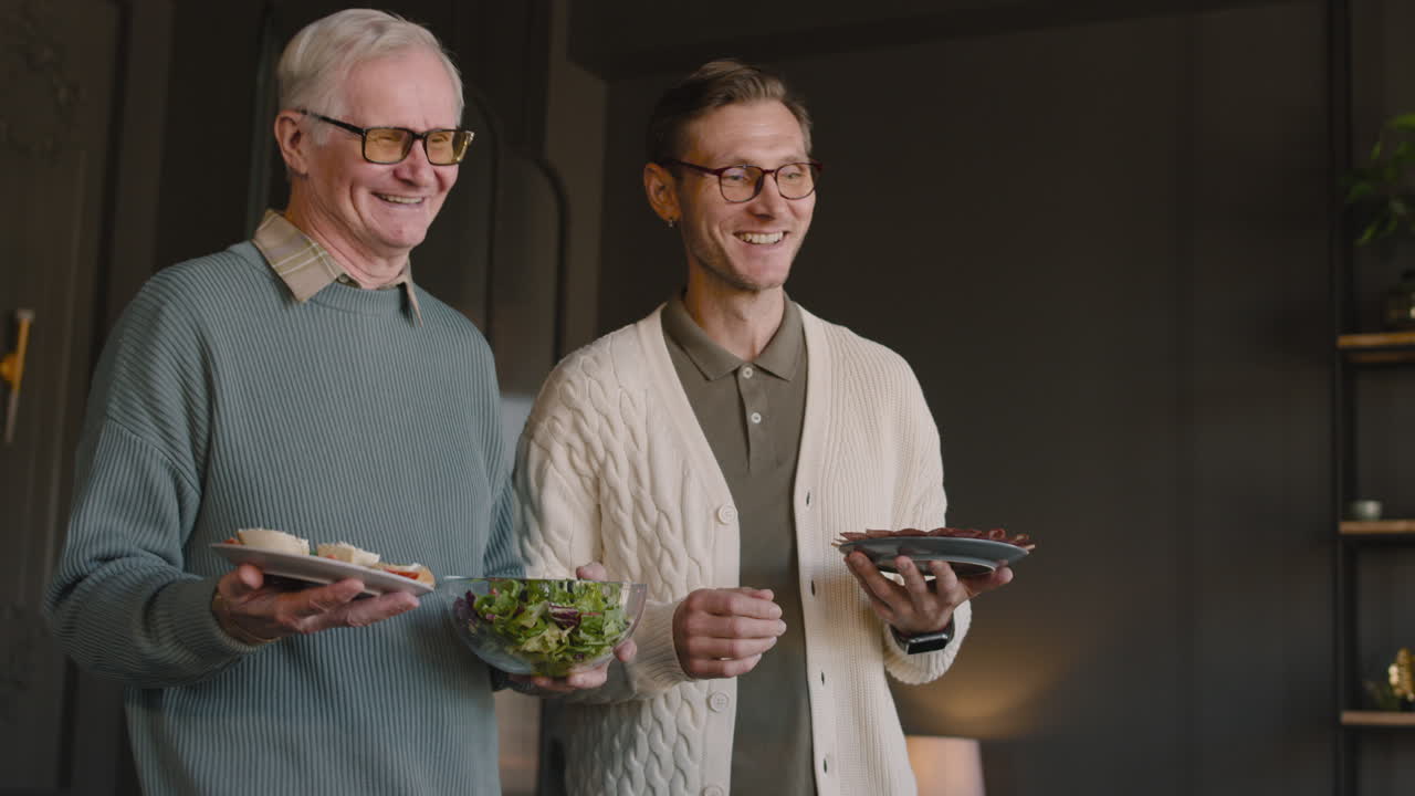 dos hombres sirviendo comida en la mesa del comedor mientras tienen una reunión familiar en casa
