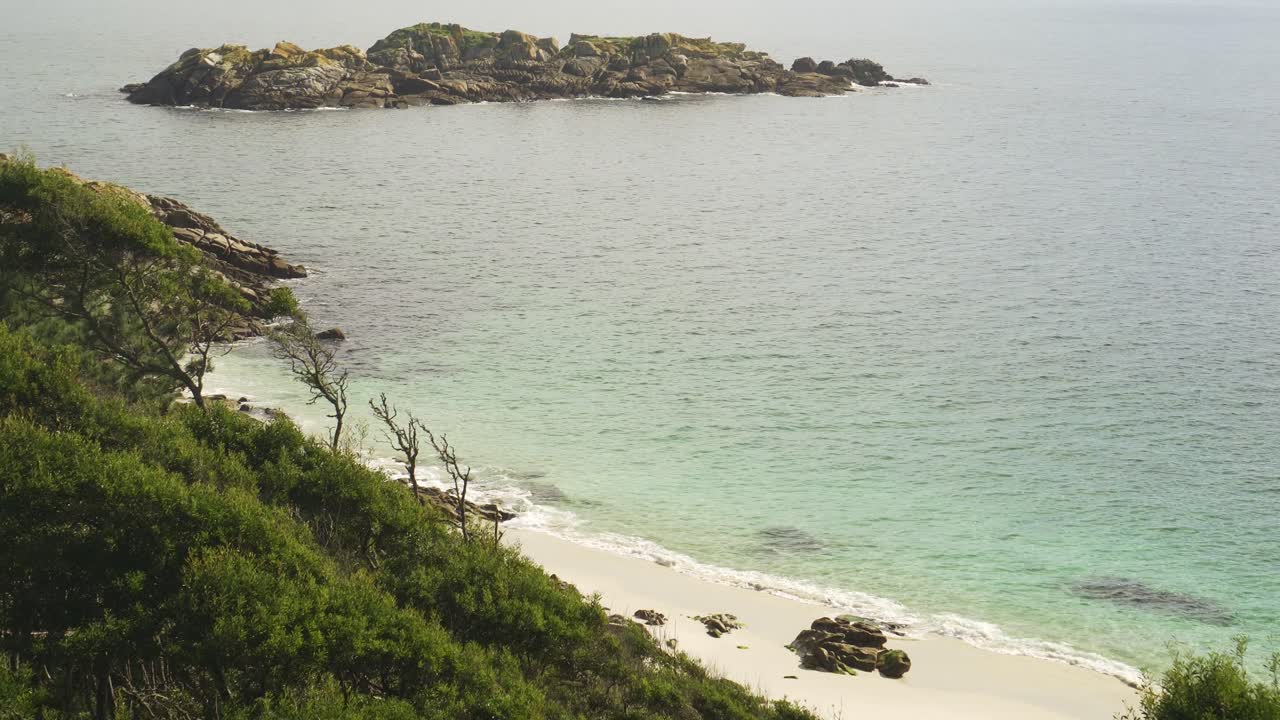 Static shot of a secret beach in the green nature with an island in the paradise of the Cíes Islands.
