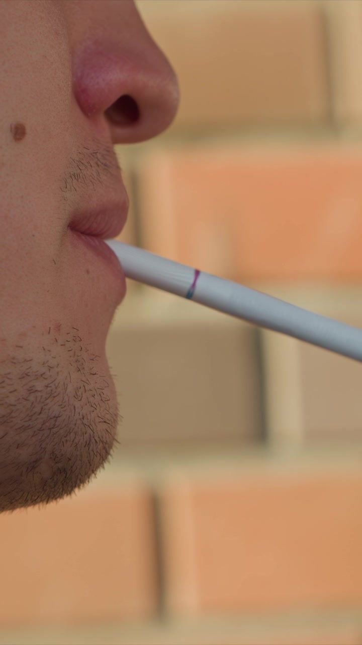 Primo piano di uomo che espira vapore da una sigaretta elettronica. I tratti del viso del soggetto e il dispositivo vape bianco sono visibili con lievi movimenti che indicano cambiamenti nella respirazione o nella posizione delle labbra