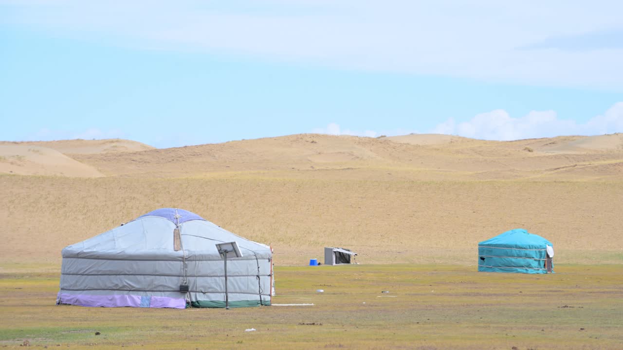 Close-up shot captures a small nomadic encampment, including a rare blue ger, nestled against vast sand dunes in the remote Mongolian desert, showcasing a traditional lifestyle