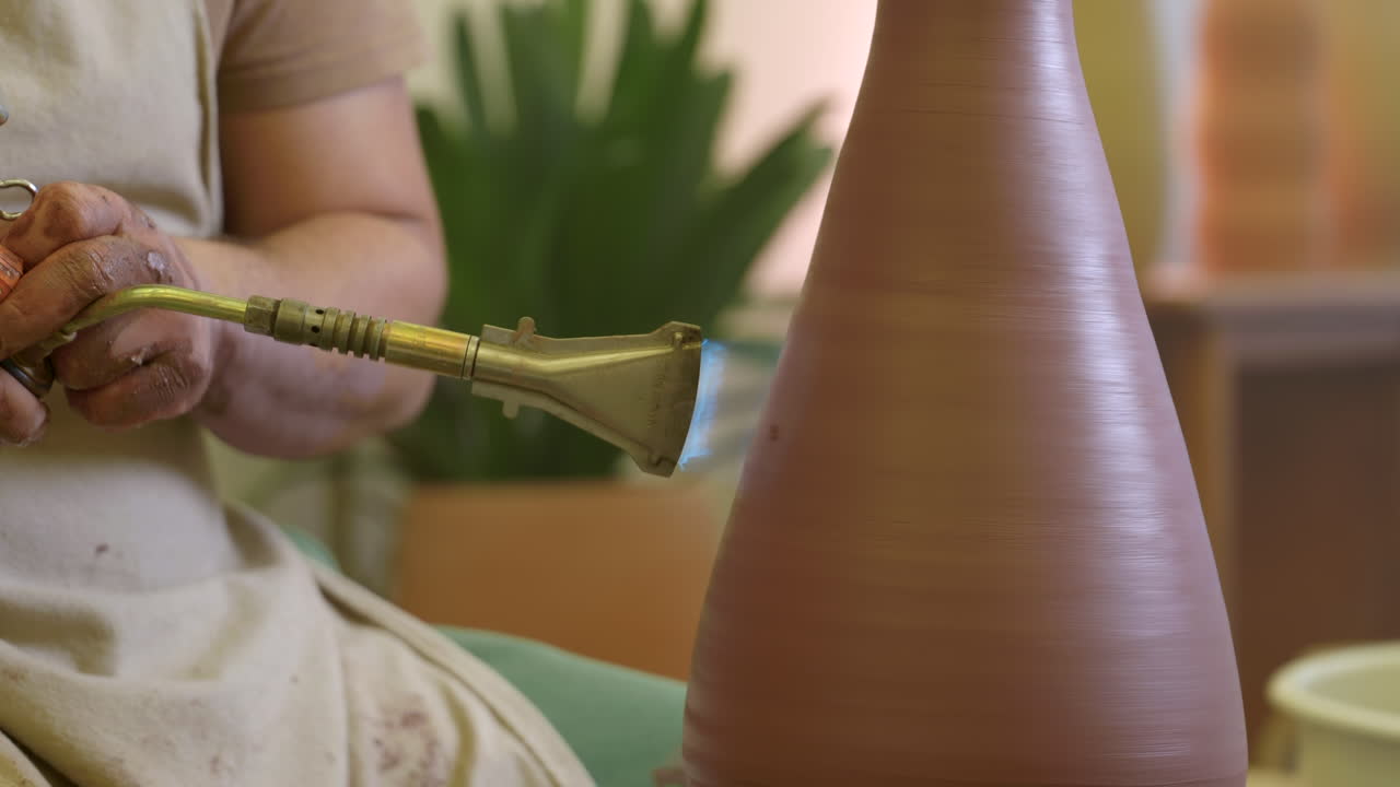 мужские руки гончаря с использованием пропанного факела для остекления глиняной вазы в студийной мастерской