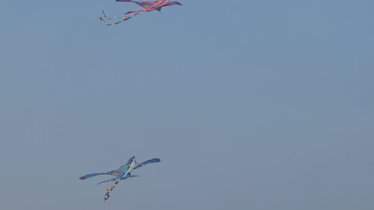 Two vibrant kites gracefully maneuver through a serene blue sky, showcasing dynamic aerial movements.