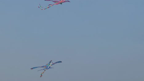 two vibrant kites gracefully maneuver through a serene blue sky, showcasing dynamic aerial movements.