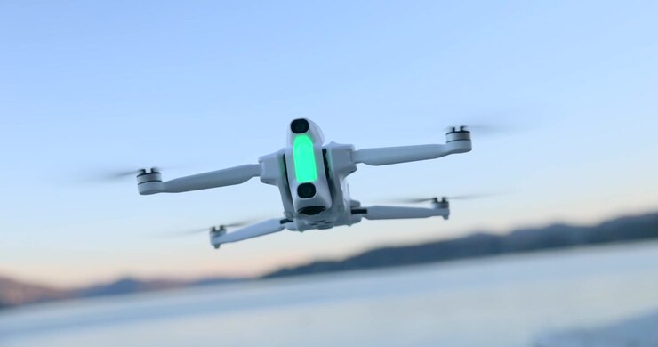 Close up of white compact drone hovering in mid-air over lake water at sunset