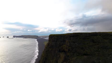 toma aérea reveladora de una playa volcánica de arena negra desde detrás de un acantilado en islandia.