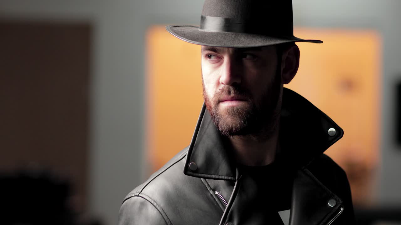 모자를 쓴 그늘진 남자가 카메라를 올려다보고, 그 뒤를 보고, 다시 카메라를 쳐다본다.