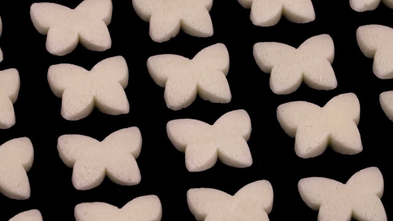 Small butterfly shaped white candies rotating. Isolated on the black background.