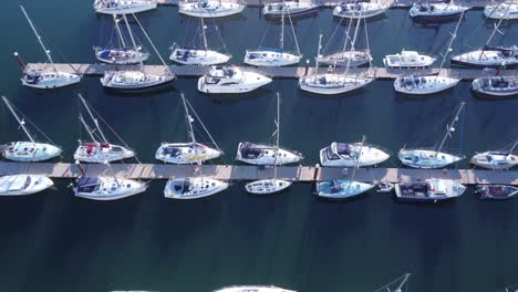 a forward flying drone shot of above and over many marina pontoons with sailing yachts and motorboats tied to them