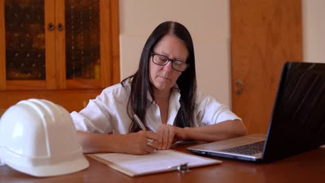 ingeniera mujer tomando notas mientras usa una computadora portátil en el escritorio