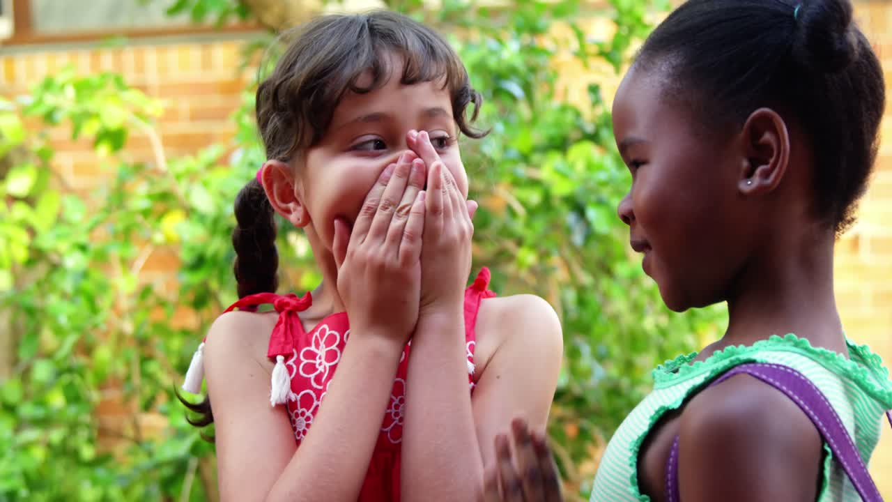 학교 캠퍼스에서 친구의 귀에 속삭이는 여학생
