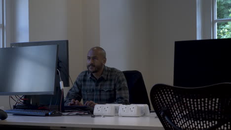 an asian businessman walking up to his office desk and sitting down in front of his computer and begins to type away on his keyboard responding to an email