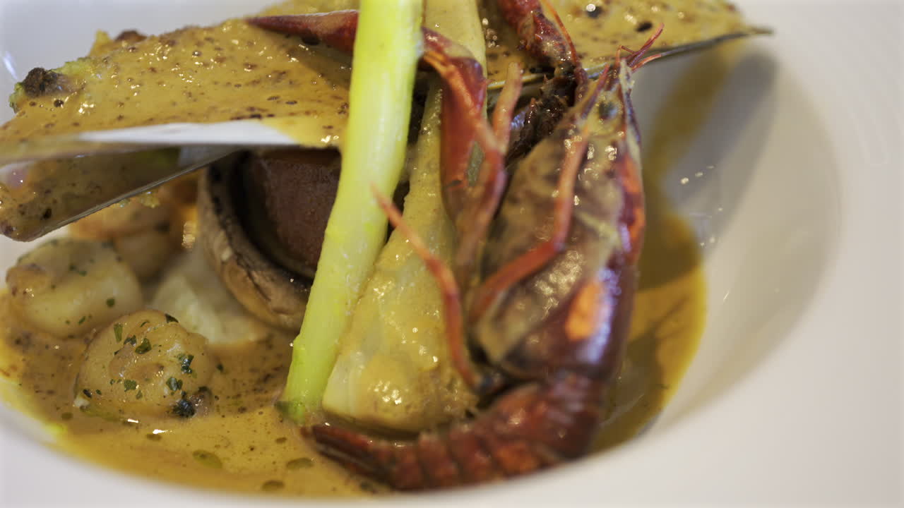 Close up of whole cooked crayfish with a mussel shell filled and a creamy herb topping on a white plate