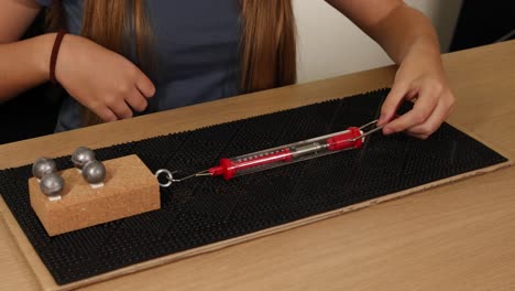 hands use a spring scale to measure force needed to drag weights on a cardboard surface, illustrating friction principles